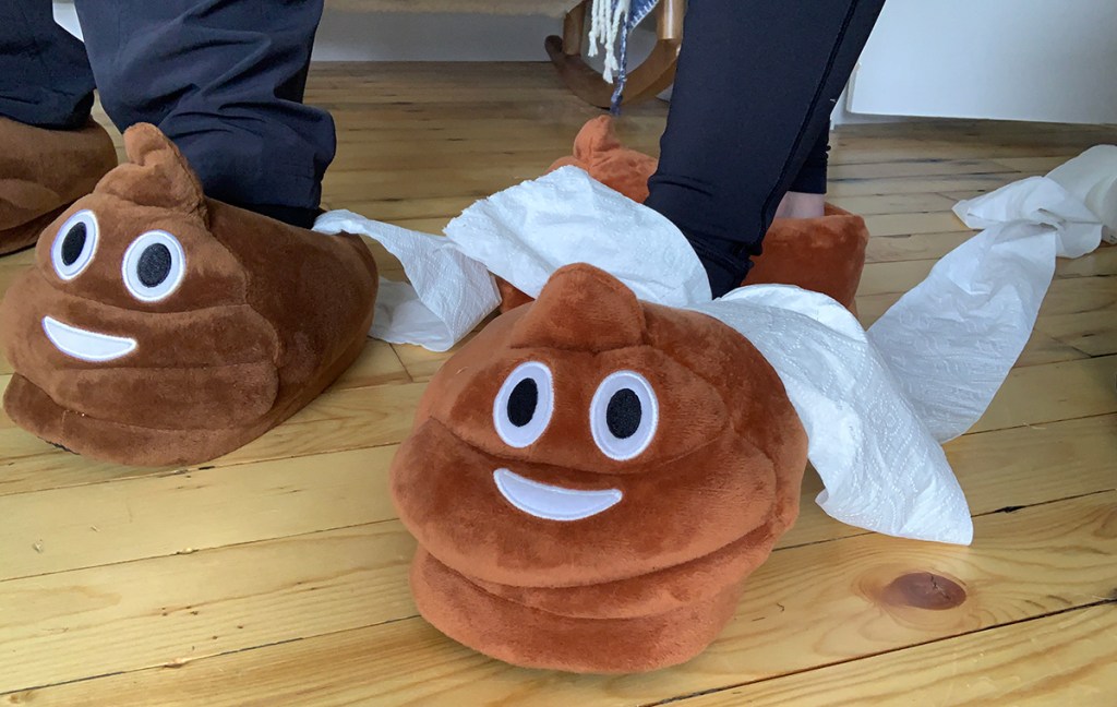 plush poop emoji slippers with toilet paper around them